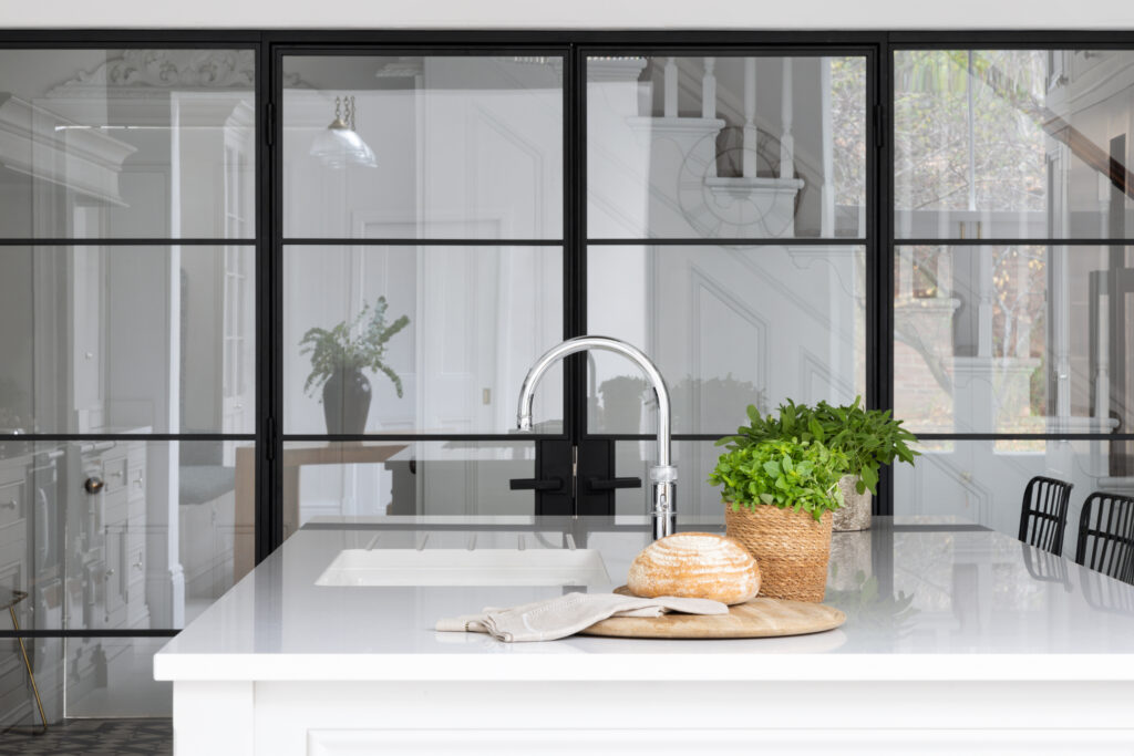 Kitchen island with sink and tap in front of black steel-framed doors opening to the hallway beyond