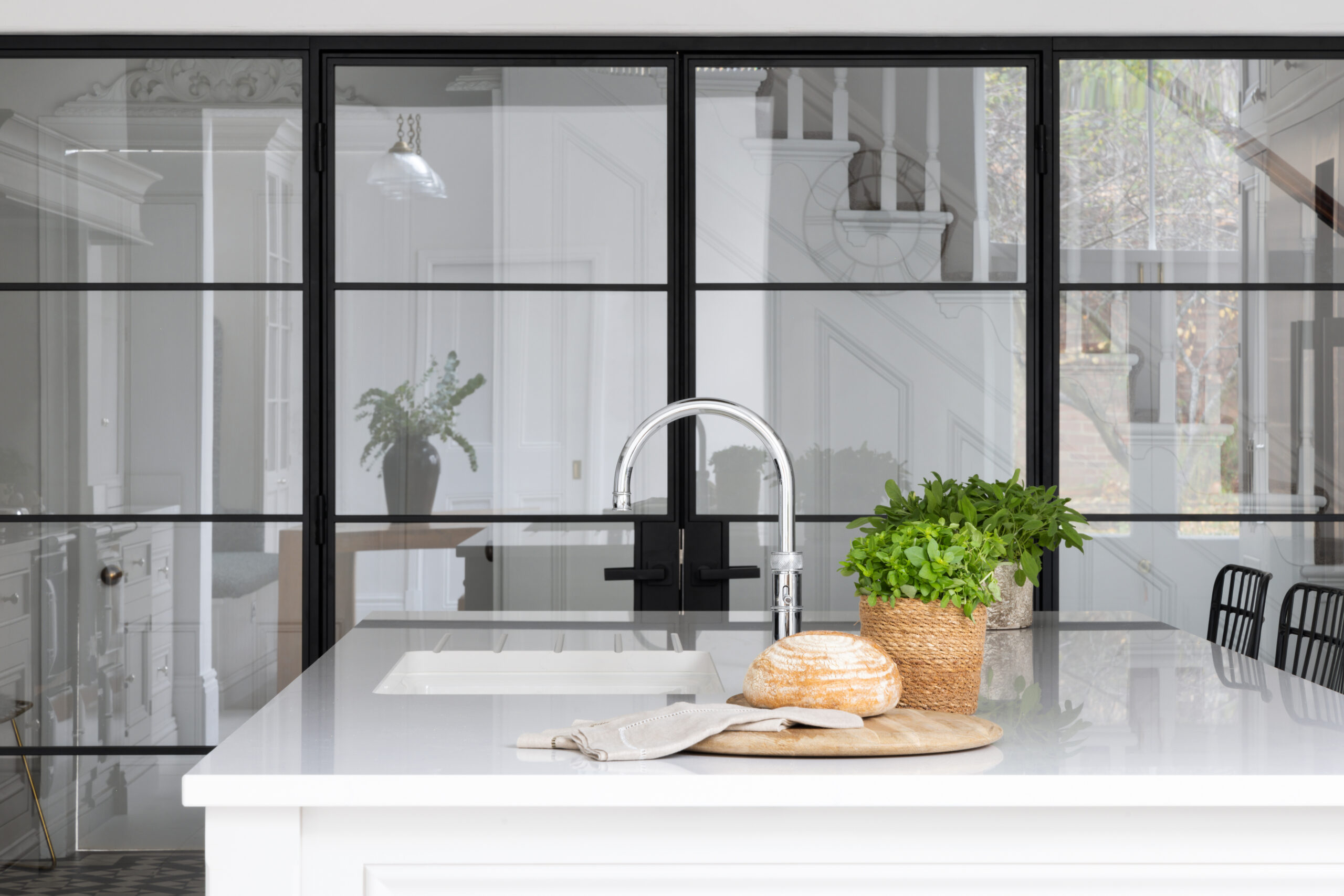 Kitchen island with sink and tap in front of black steel-framed doors opening to the hallway beyond