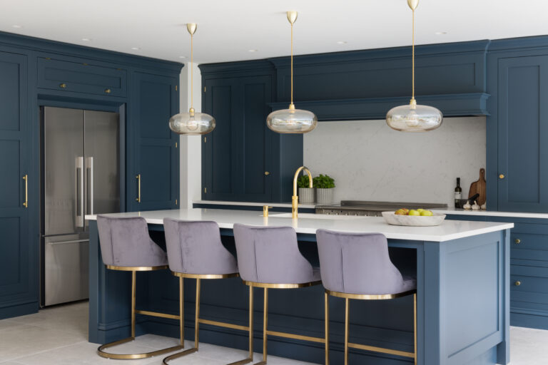 Deep blue kitchen island with velvet stools, brass pendant lights and brass tap against matching cabinetry