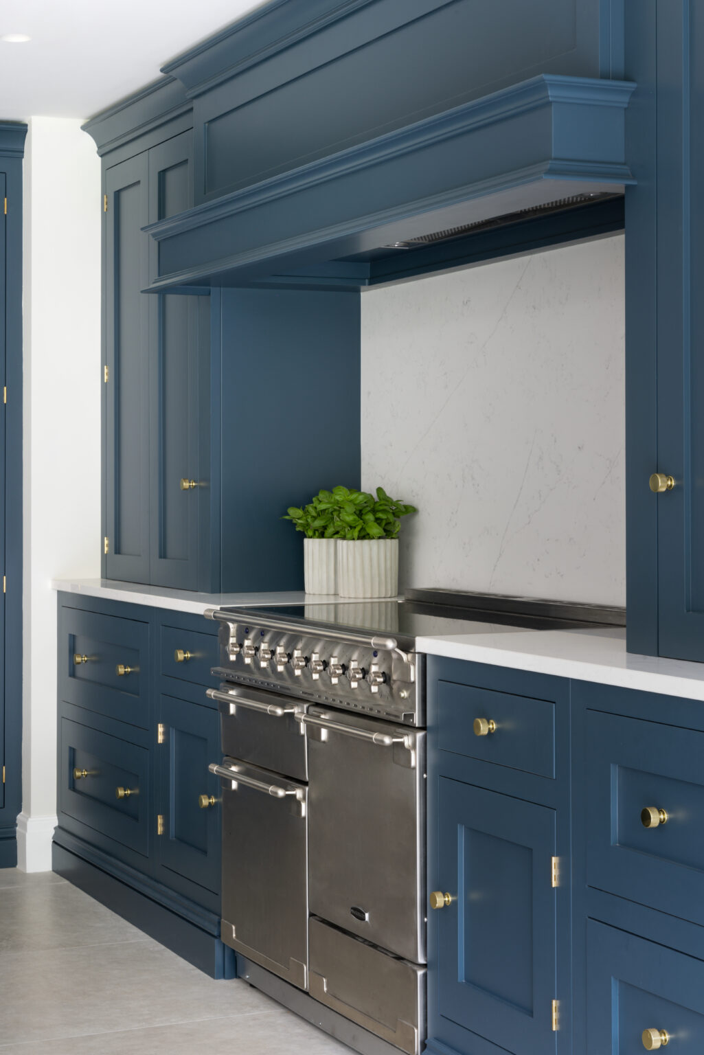Deep blue cabinetry with brass handles surrounds a stainless steel range cooker beneath a matching canopy extractor
