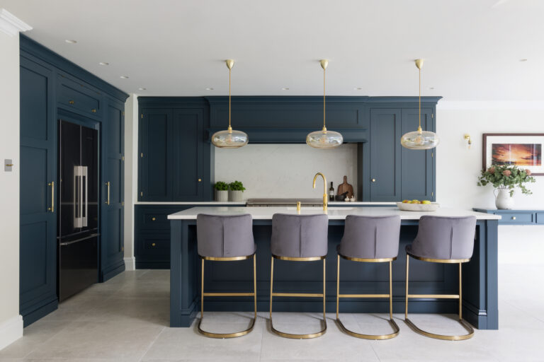 Deep blue kitchen cabinetry with brass fittings, a central island, velvet stools and brass pendant lighting above