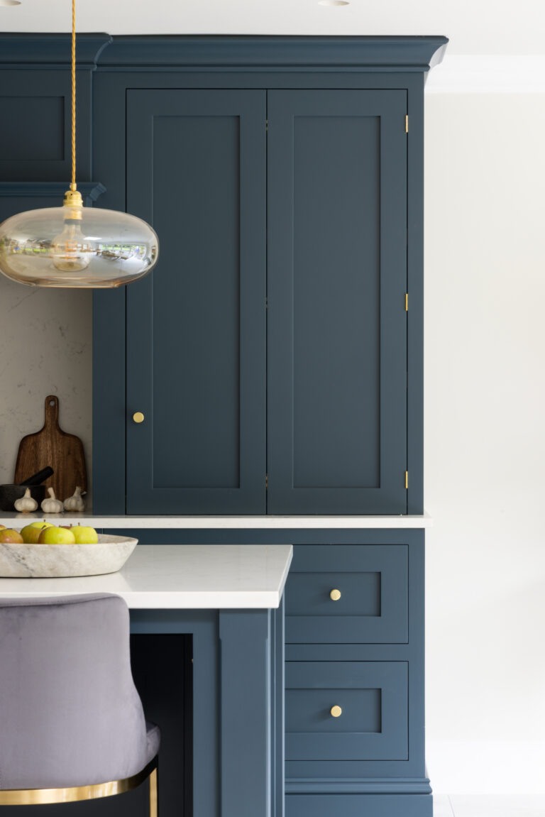 Closed bi-fold bar cabinet in Farrow & Ball Hague Blue with brass handles, above drawers and a white worktop