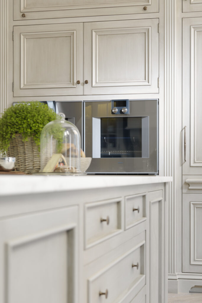 Hand-painted kitchen cabinetry with panelled doors, brass handles and an integrated oven beside a marble worktop