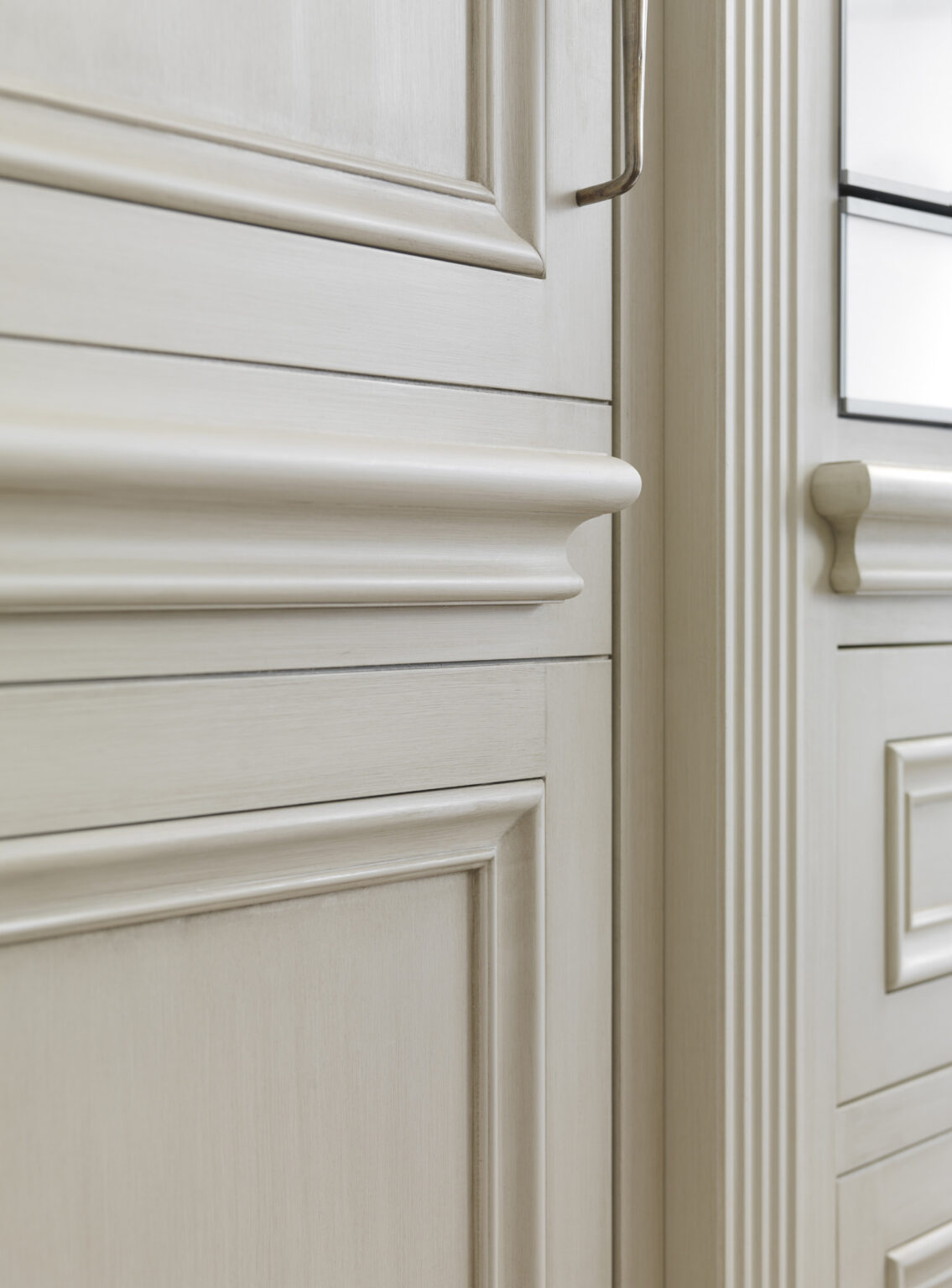 Close-up of hand-painted cabinetry showing classical moulding detail and a fluted pilaster beside a glazed cabinet door