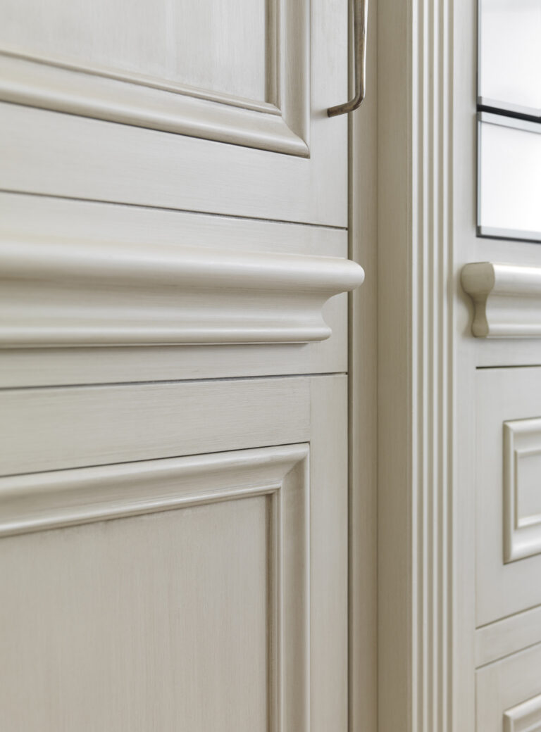 Close-up of hand-painted cabinetry showing classical moulding detail and a fluted pilaster beside a glazed cabinet door