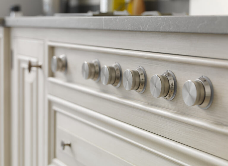 Close-up of hand-painted cabinetry with brushed metal control dials set beneath a marble worktop
