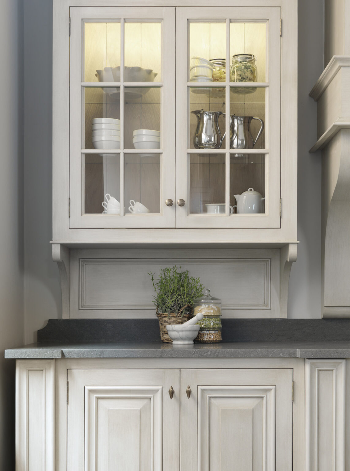 Illuminated glazed dresser cabinet with crockery, set above panelled cupboards and a dark stone worktop