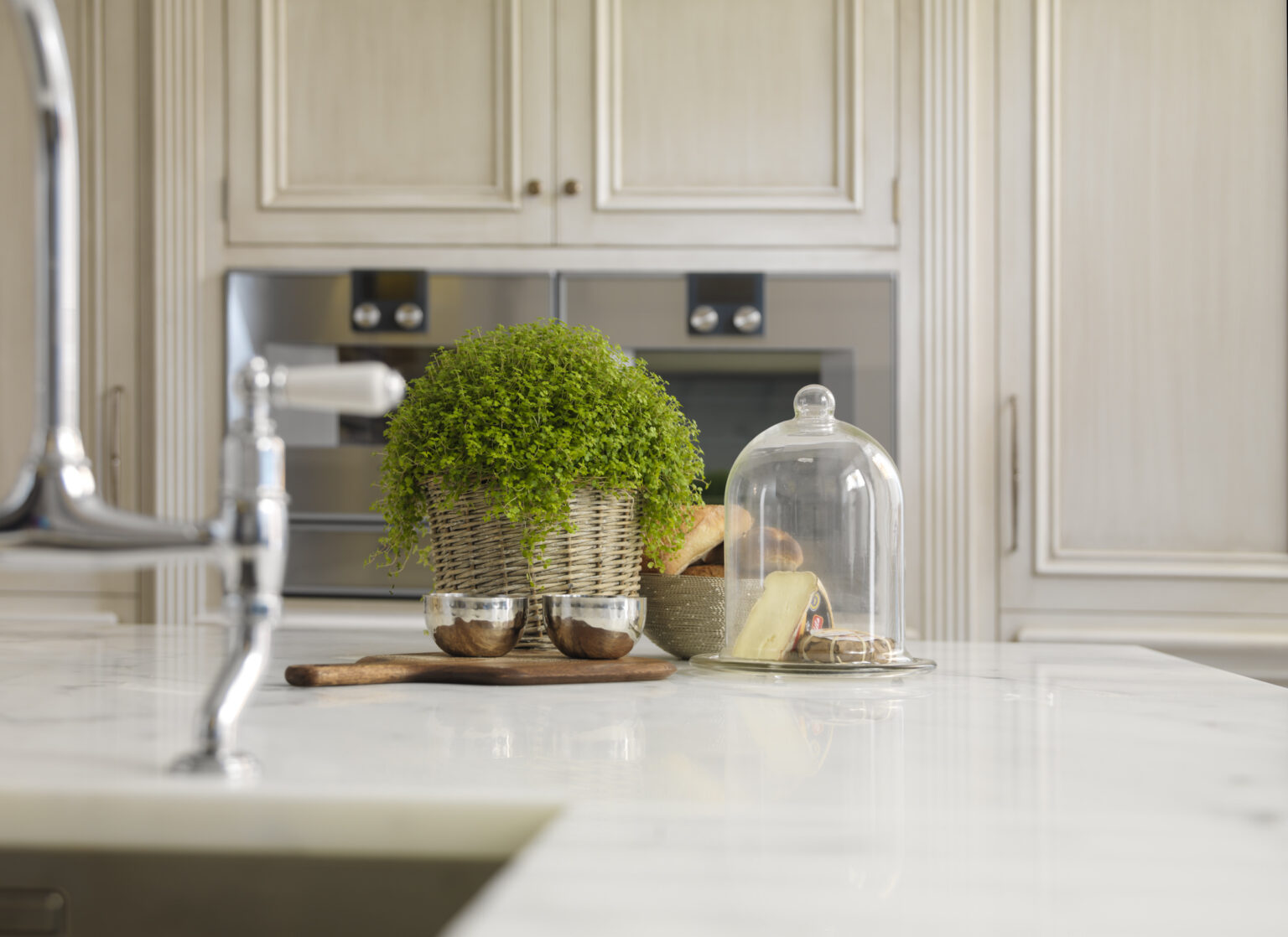 Carrara marble island with traditional tap, hand-painted cabinetry and integrated ovens in the background