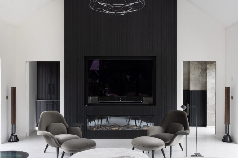 Double-height lounge with black slatted ash media wall, integrated television, fireplace and low-slung armchairs on terrazzo flooring