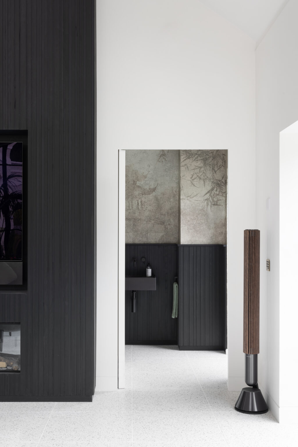 Black slatted ash media wall beside a terrazzo floor hallway leading to a cloakroom with patterned panelling