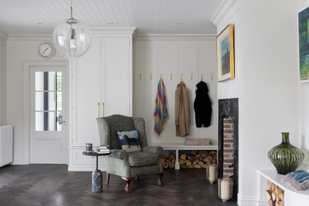 Boot room with panelled cupboards, brass coat hooks, a bench and armchair beside an old fireplace