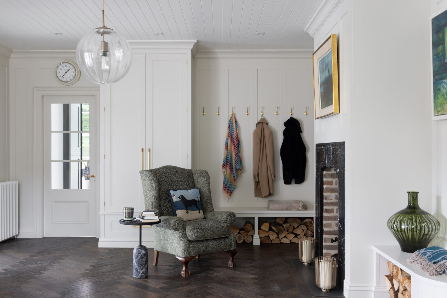 Boot room with panelled cupboards, brass coat hooks, a bench and armchair beside an old fireplace