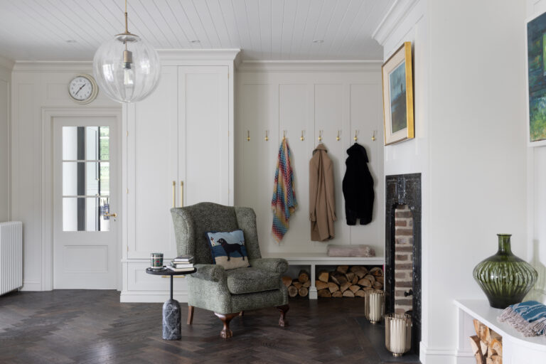 Boot room with panelled cupboards, brass coat hooks, a bench and armchair beside an old fireplace