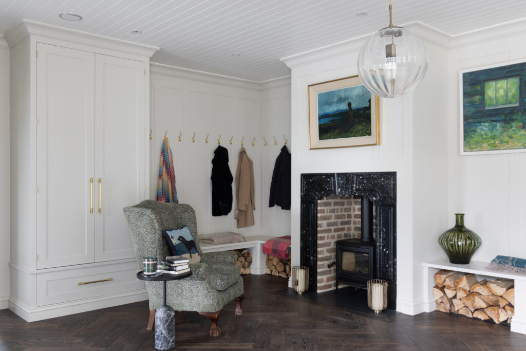 Boot room with panelled cabinetry, brass hooks, bench seating and a wood-burning stove within a fireplace