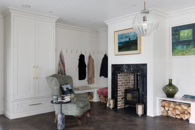 Boot room with panelled cabinetry, brass hooks, bench seating and a wood-burning stove within a fireplace