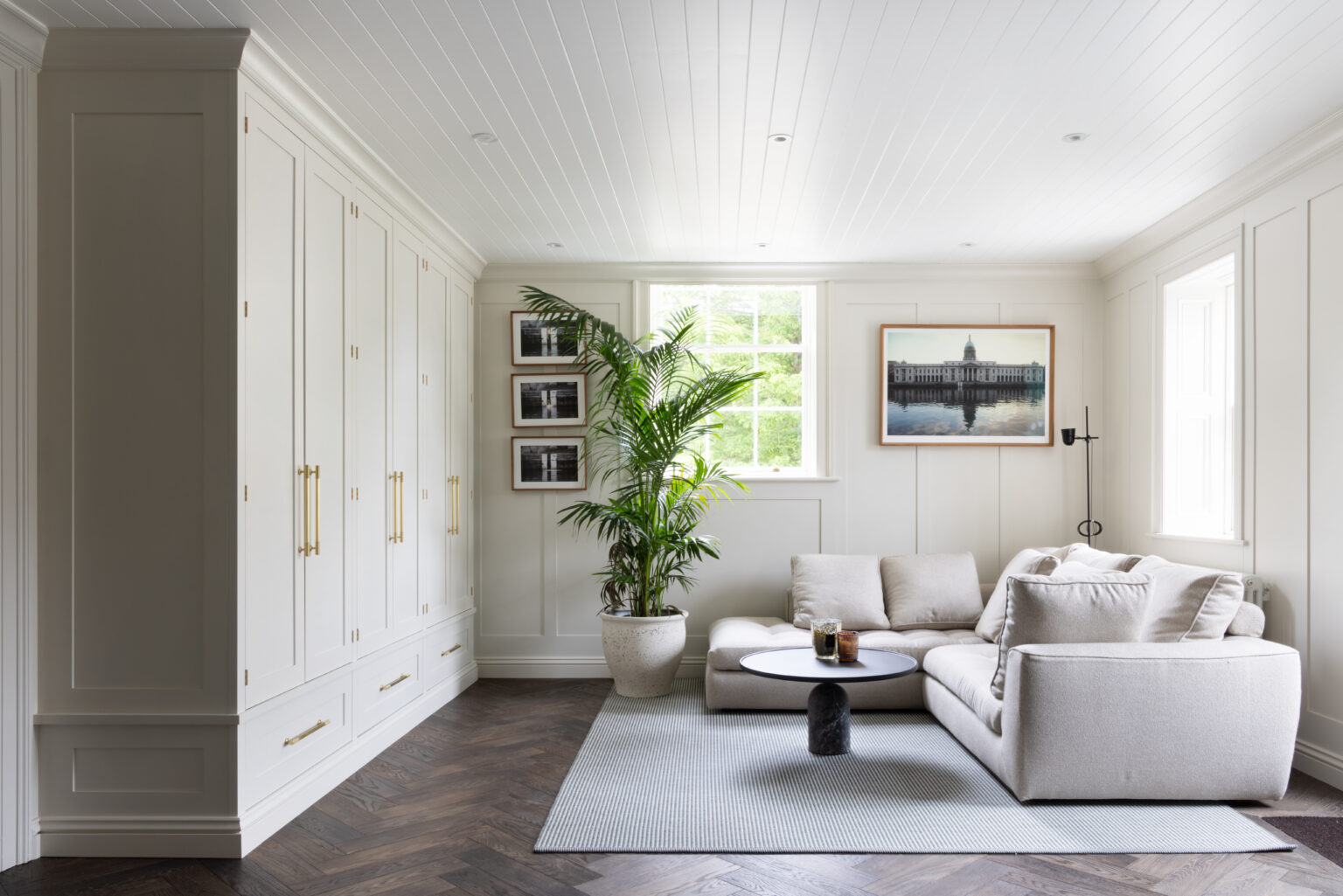 Sitting room with fitted painted wardrobes, brass handles, a corner sofa and dark herringbone parquet flooring