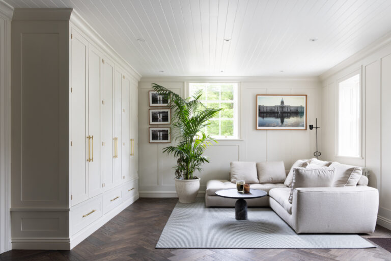 Sitting room with fitted painted wardrobes, brass handles, a corner sofa and dark herringbone parquet flooring