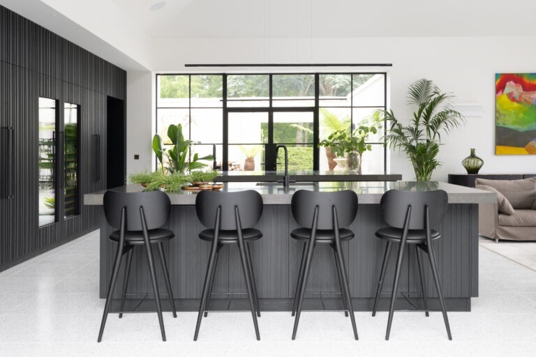 Open-plan kitchen with a large fluted island, four black bar stools and a wall of crittall-style windows