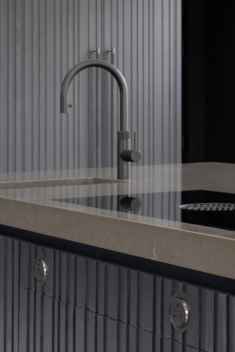 Close-up of a kitchen island with a curved stone worktop, integrated sink, induction hob and a brushed steel mixer tap