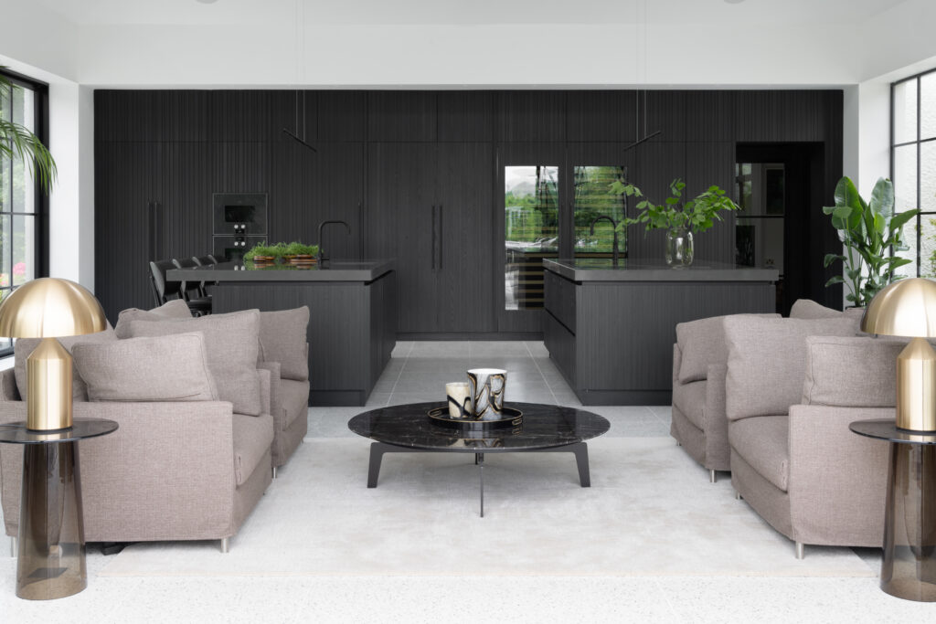 Open-plan living space with dark ribbed kitchen cabinetry, twin islands and armchairs facing a round coffee table