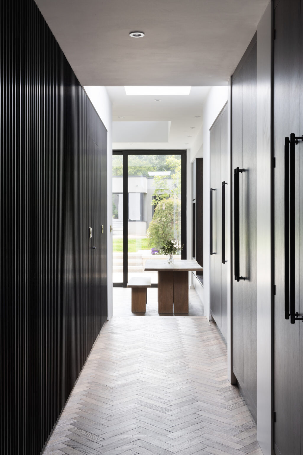 Hallway with fluted panelled storage, herringbone flooring and a wooden table leading to the garden doors