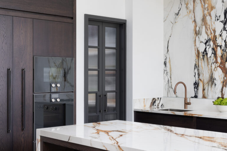 Kitchen with dark timber cabinetry, built-in ovens, a striking veined stone wall and matching island worktop with copper tap