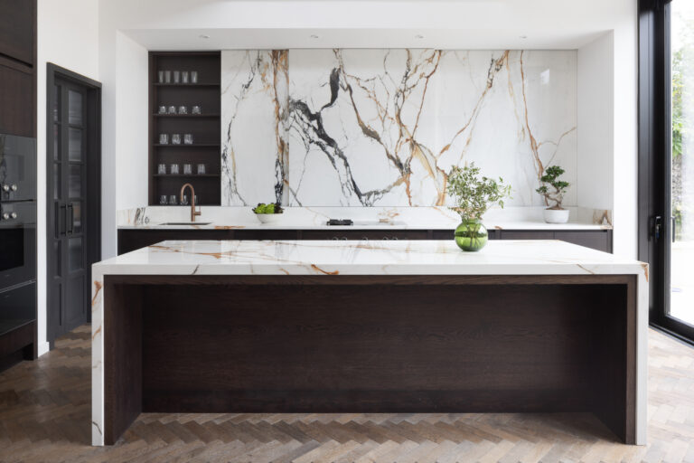 Open-plan kitchen island with dark cabinetry, waterfall stone worktop and matching veined stone wall behind