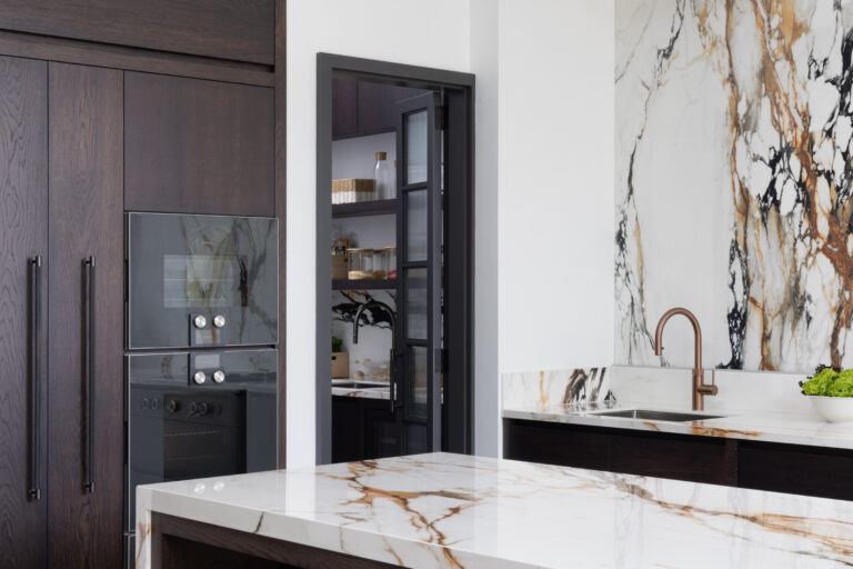 Open-plan kitchen with a striking wall of moving stone, copper tap and glazed door opening to a hidden walk-in pantry