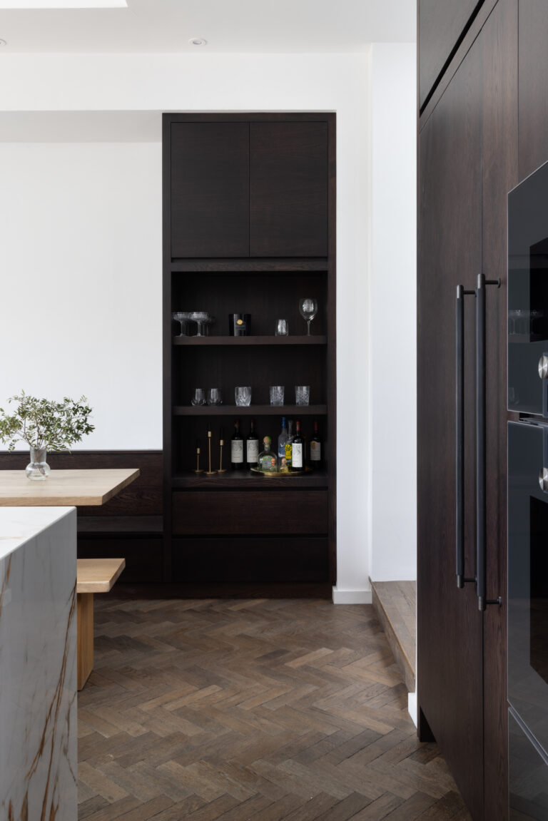 Dark built-in drinks cabinet with open shelving for glassware and bottles above herringbone parquet flooring