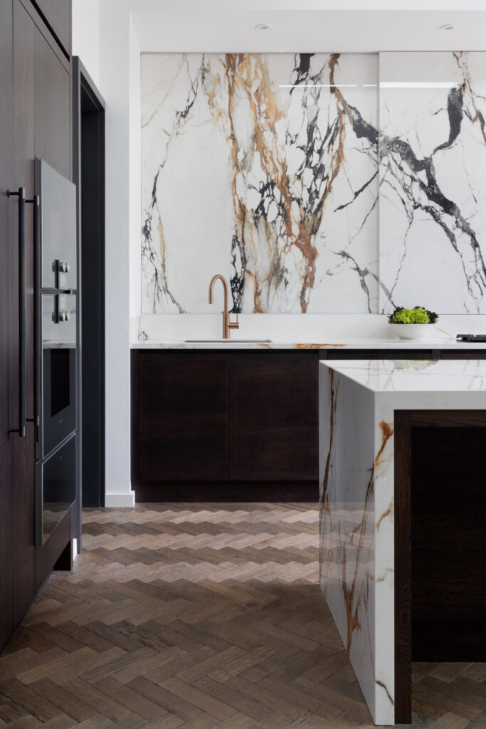 Kitchen with a striking veined stone wall, copper tap, dark cabinetry and herringbone wood flooring