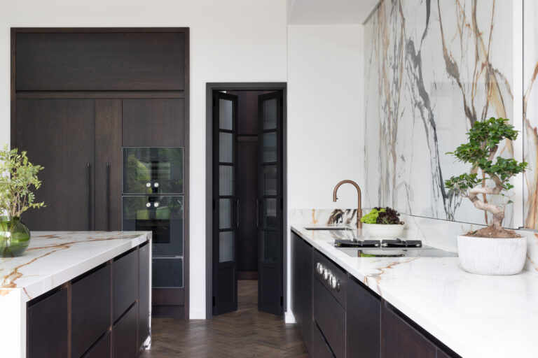 Open-plan kitchen with dark cabinetry, a moving stone splashback wall, copper tap and herringbone wood flooring