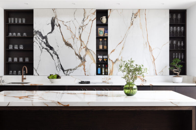 Open-plan kitchen with a striking wall of moving stone, dark cabinetry, open shelving and an island with glassware and plants