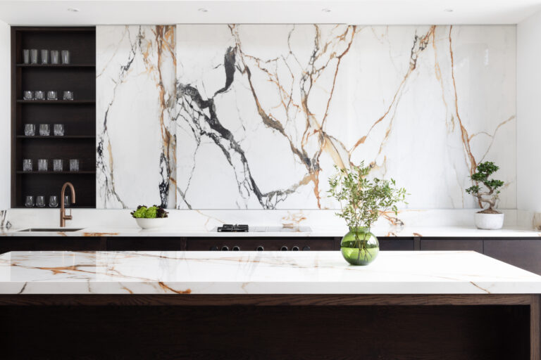 Kitchen island with veined stone worktop, dark cabinetry, built-in glassware shelving and a copper tap