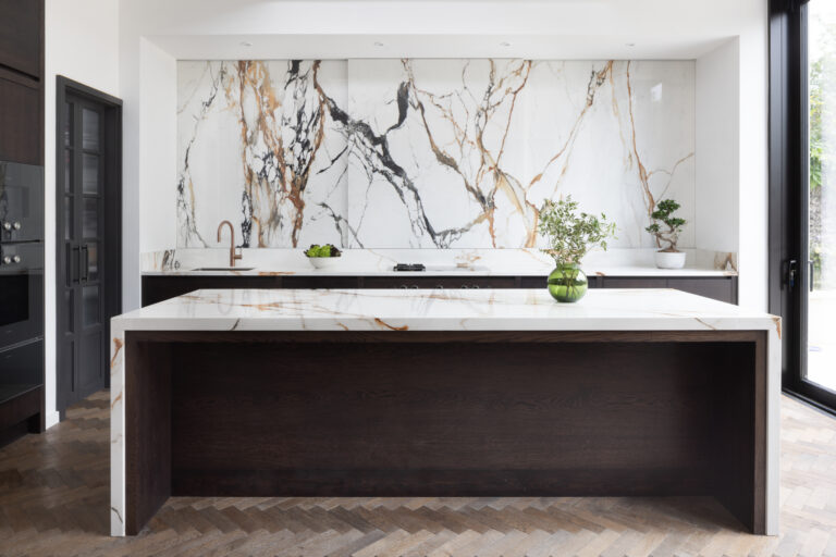Open-plan kitchen with dark timber island, veined stone worktop and matching wall of moving stone behind
