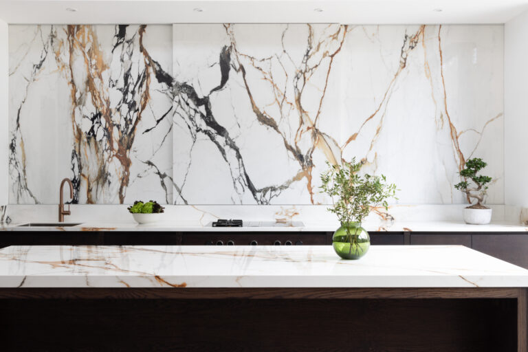 Kitchen with a dramatic veined stone wall above dark cabinetry, matching island worktop, and a copper tap