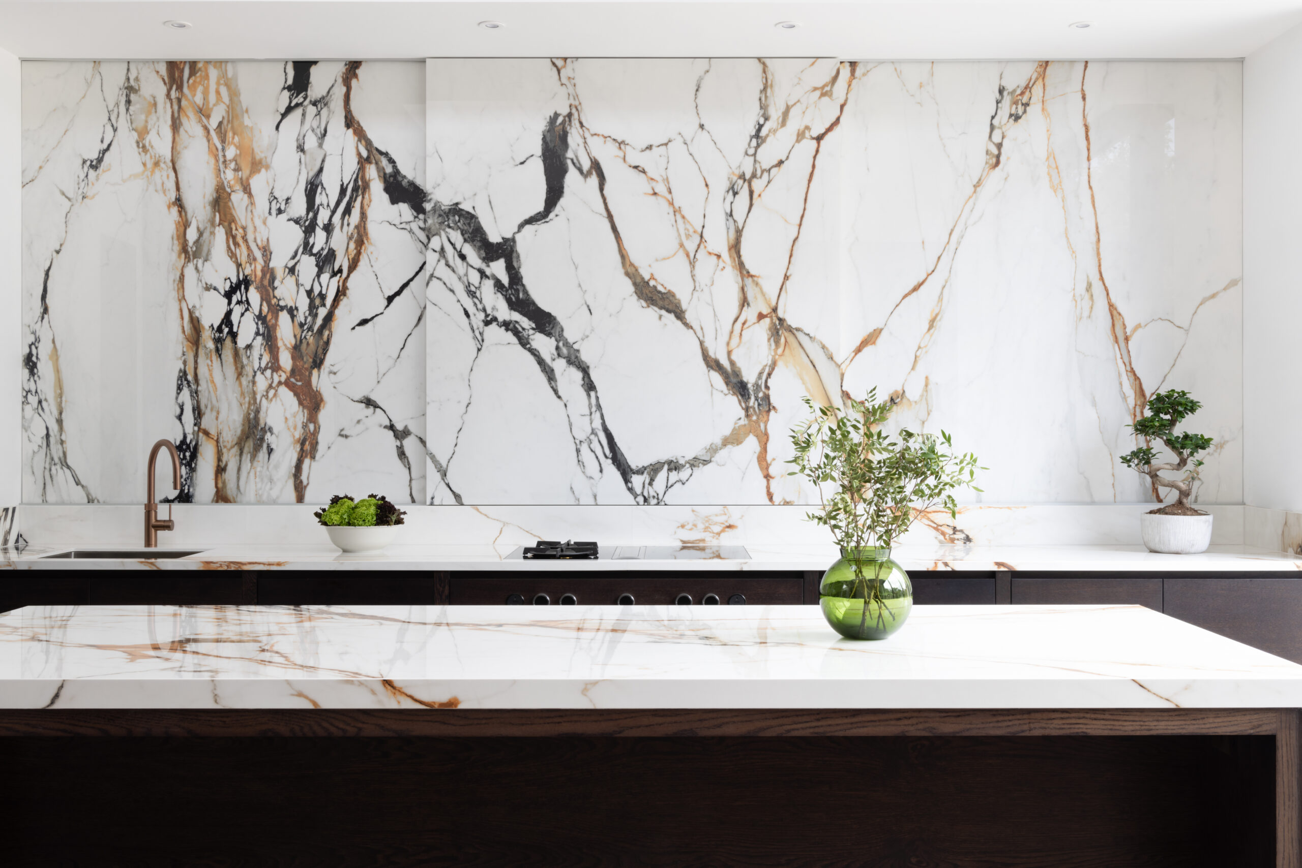 Kitchen with a dramatic veined stone wall above dark cabinetry, matching island worktop, and a copper tap