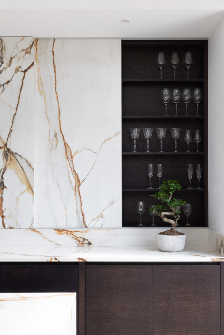 Sliding XTONE Paonazzo Biondo stone panel beside open dark timber shelving displaying glassware and a small potted plant