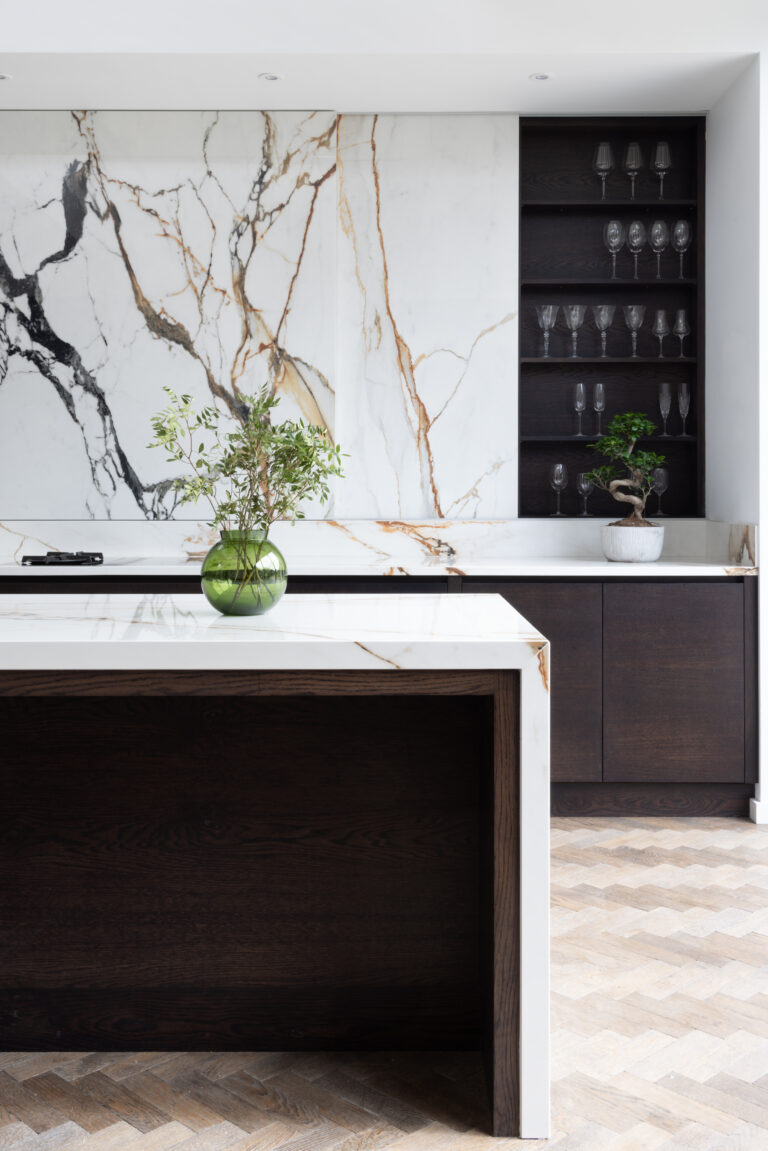 Kitchen island with dark cabinetry beside a XTONE Paonazzo Biondo stone wall and open glassware shelving
