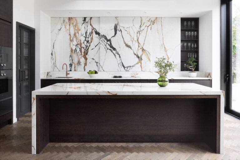 Open-plan kitchen with large island, dark cabinetry, a dramatic moving stone wall and herringbone wood flooring