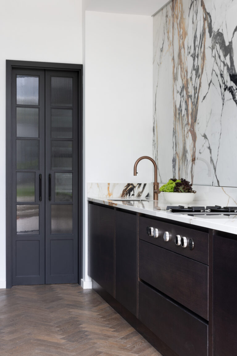 Dark cabinetry sits beneath a wall of XTONE Paonazzo Biondo stone, with a fluted glass pantry door alongside