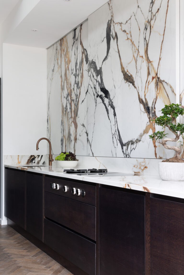Dark cabinetry beneath a worktop and wall clad in XTONE Paonazzo Biondo stone, with a copper tap and gas hob