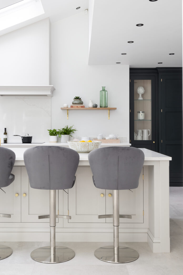 Kitchen island with grey velvet bar stools, floating shelf and dark glazed cabinetry in the background