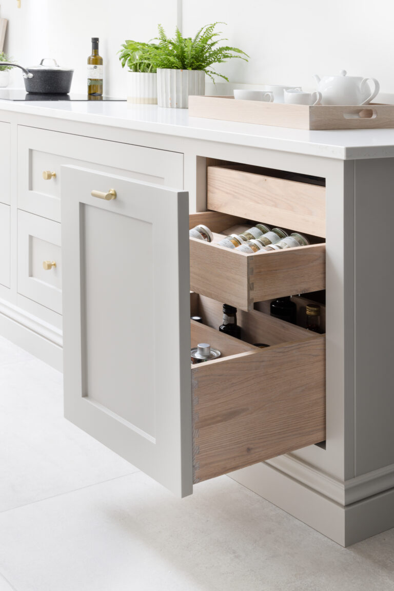 Deep pan drawers with brass handles open to reveal jars and bottles beneath a white worktop