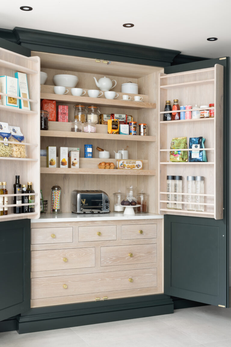 Open larder cupboard with dark cabinetry, internal shelving, brass knobs and drawers storing crockery, groceries and a toaster