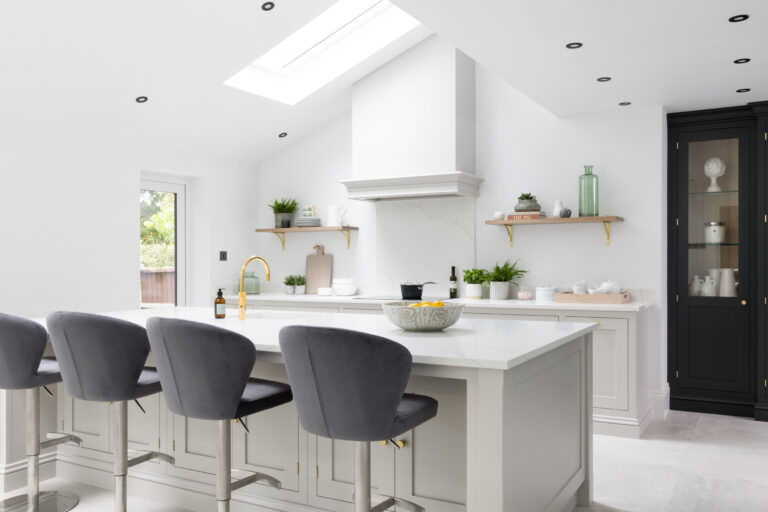 Bright kitchen with a large island, grey velvet bar stools, floating shelves and a skylight above the cooker hood