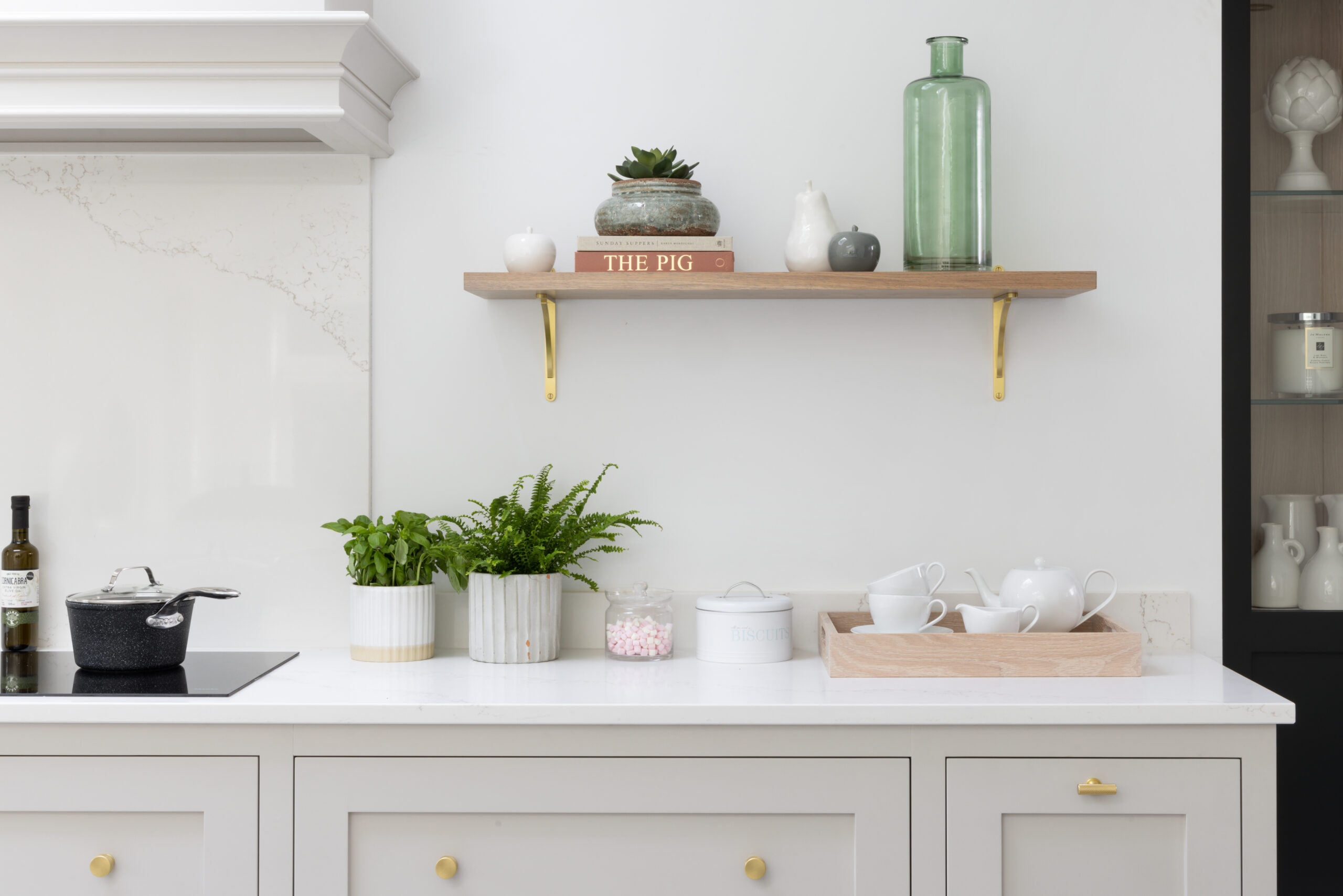 Floating timber shelf with brass brackets above a worktop styled with plants, books and a tea tray