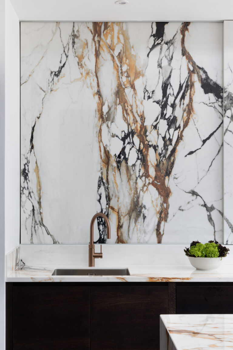 Kitchen sink with copper tap set against the striking wall of moving stone and dark cabinetry below