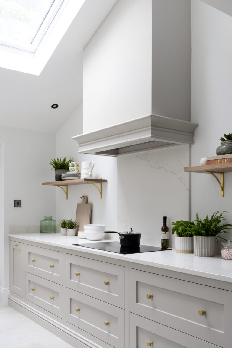 Kitchen with deep pan drawers, brass handles, floating shelves and an induction hob beneath a panelled extractor canopy