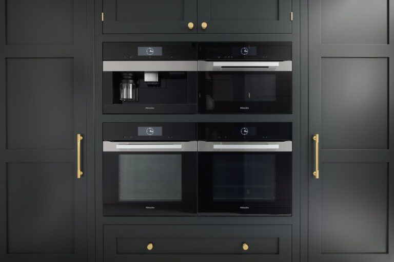 Dark cabinetry houses four built-in Miele appliances, including a coffee machine, with brass handles and knobs