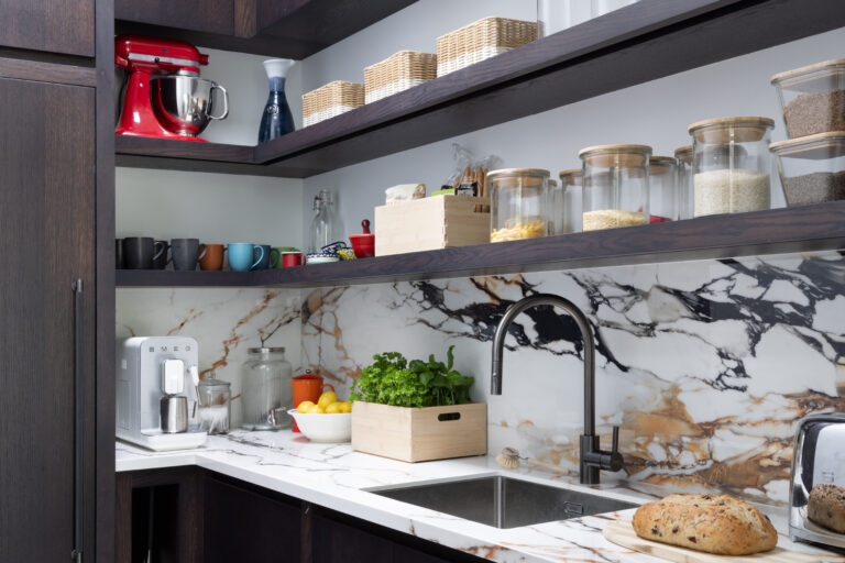 Pantry shelving with a sink, striking moving stone splashback, and open shelves holding jars, mugs and baskets